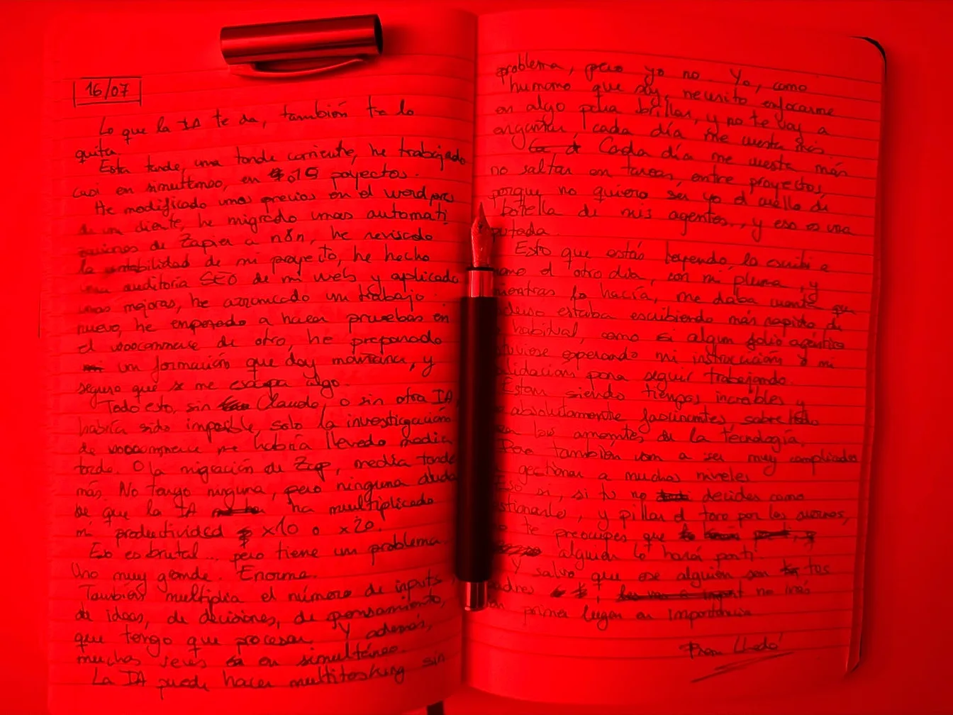 Una libreta abierta con este ensayo escrito a mano a doble página y una pluma estilográfica en el centro, todo bañado por una luz roja.